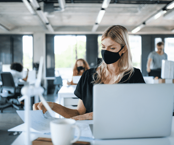 woman in face mask working on laptop at desk