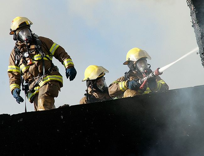 Three firefighters on burn tower running a hose for ISO training requirements